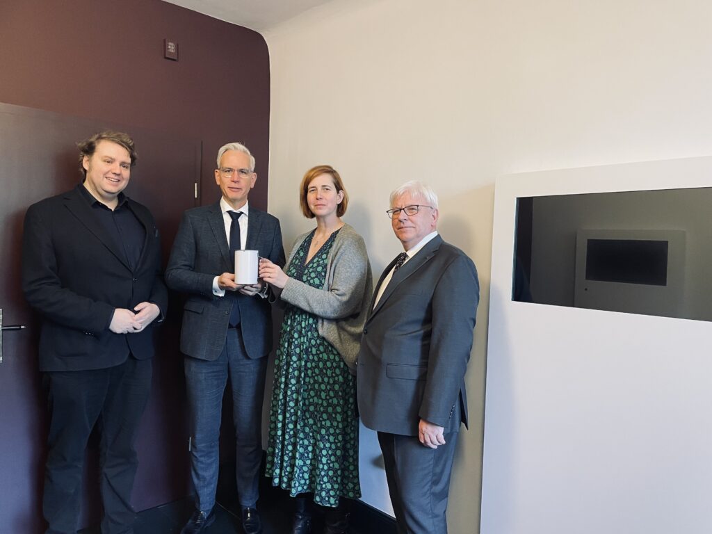 Drei Männer und eine Frau stehen in den Räumen der zukünftigen neuen Dauerausstellung der Villa Merländer und halten eine Spendendose in der Hand