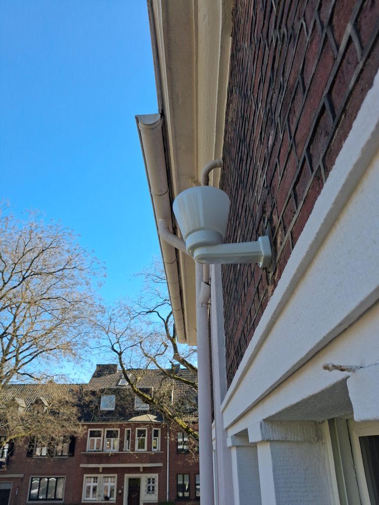 Die Außenfassade eines Hauses mit einer antiken Lampe. Im Hintergrund sind der blaue Himmel und weitere Häuser zu sehen