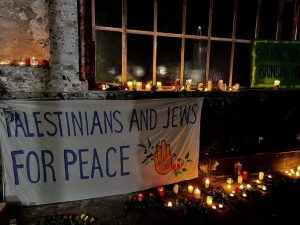 Ein Plakat mit der Aufschrift Palästinians and Jews for Peace" hängt vor zahlreichen brennenden Kerzen