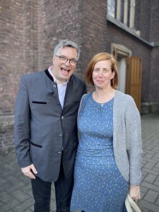 Ein Mann und eine Frau stehen vor einem Gebäude und lachen in die Kamera